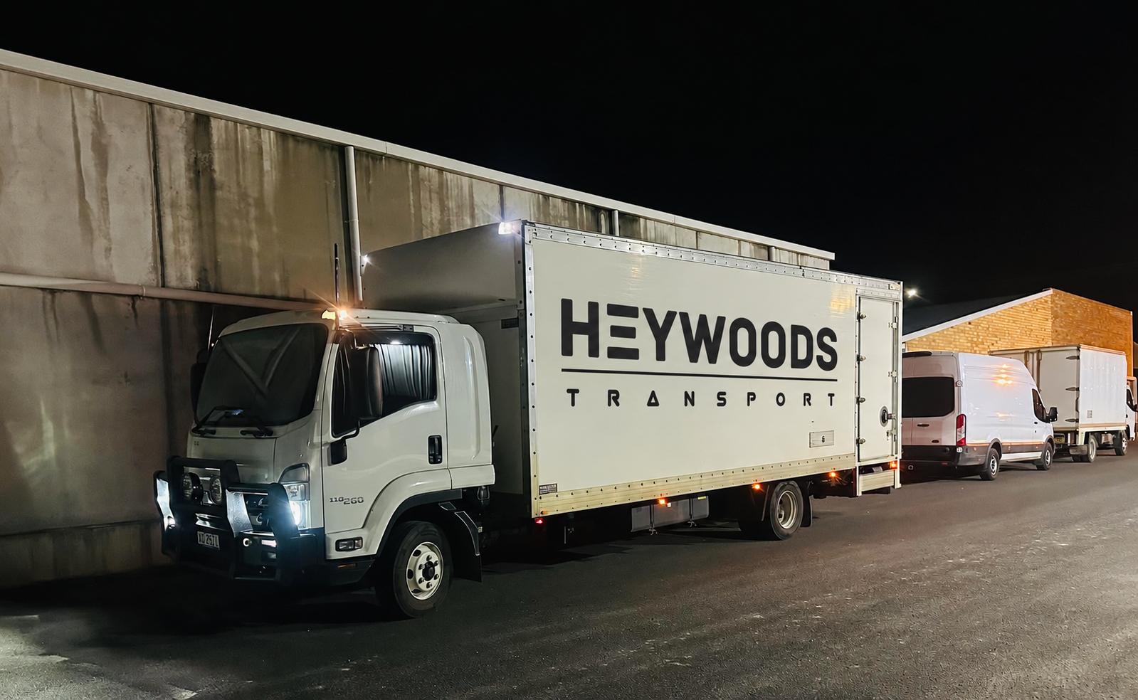 Concept image of a Heywoods Transport truck with the company logo on its side, parked at night