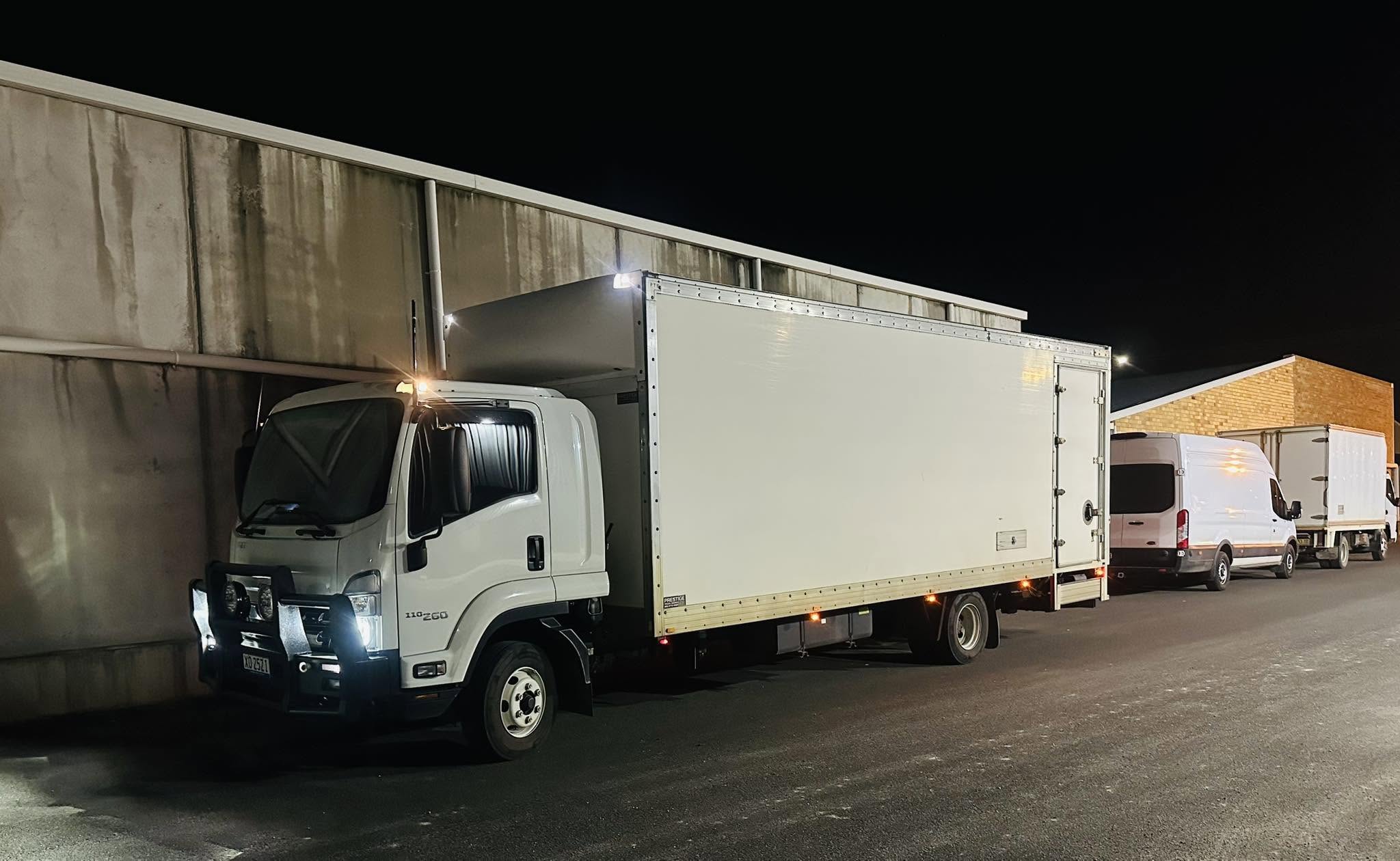 Heywoods Transport truck and delivery vehicles parked together at night